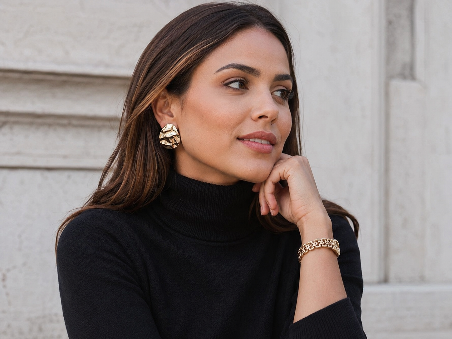 Gola alta preta combinada com brinco dourado e pulseira, sem acessórios no pescoço.